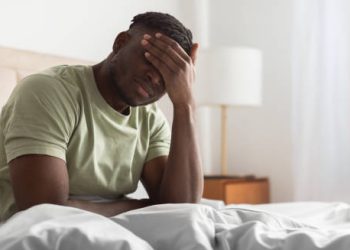 Man sitting on bed with hand on face, experiencing pain from Ehlers-Danlos Syndromes complications.