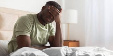 Man sitting on bed with hand on face, experiencing pain from Ehlers-Danlos Syndromes complications.