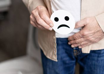 Elderly man holding sad face icon near pelvis, indicating urinary issues from enlarged prostate