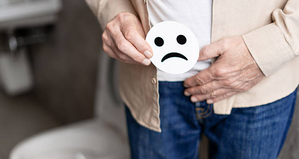 Elderly man holding sad face icon near pelvis, indicating urinary issues from enlarged prostate