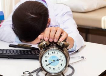 Tired doctor resting at desk with alarm clock and stethoscope