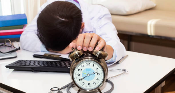 Tired doctor resting at desk with alarm clock and stethoscope