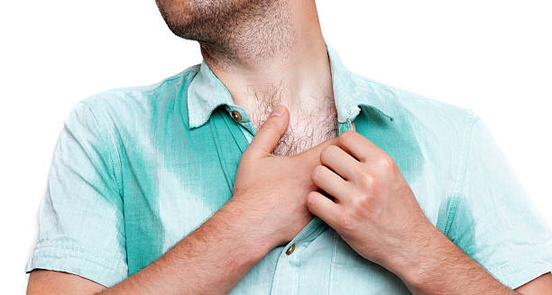 Man with sweat-soaked shirt scratching chest due to excessive sweating