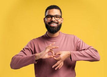 Smiling man using sign language against a yellow background