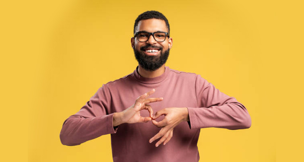 Smiling man using sign language against a yellow background