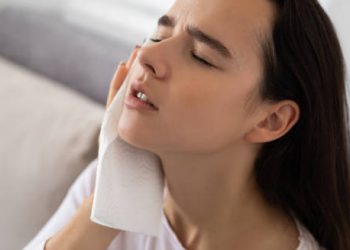 Woman holding a cloth to her face, appearing fatigued and unwell