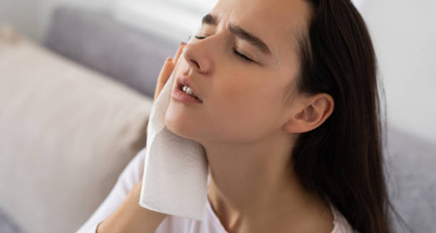 Woman holding a cloth to her face, appearing fatigued and unwell