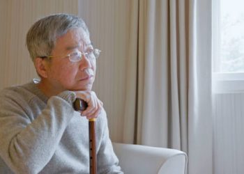 Elderly man sitting pensively with a cane in a bright room