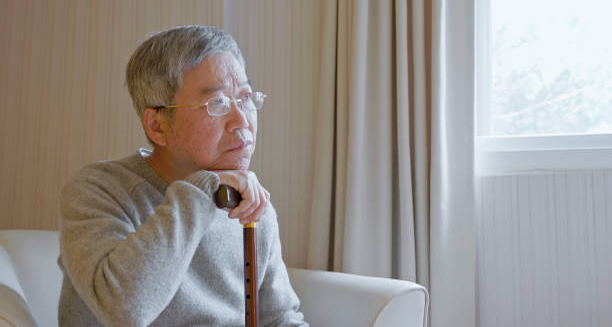 Elderly man sitting pensively with a cane in a bright room