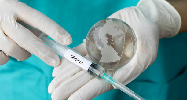 Cholera-labelled syringe held by gloved hands next to a transparent globe
