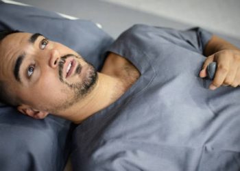 Anxious man inside MRI scanner holding emergency button, showing signs of claustrophobia.