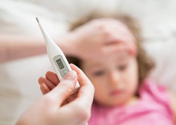 Digital thermometer showing fever in front of a sick child lying in bed