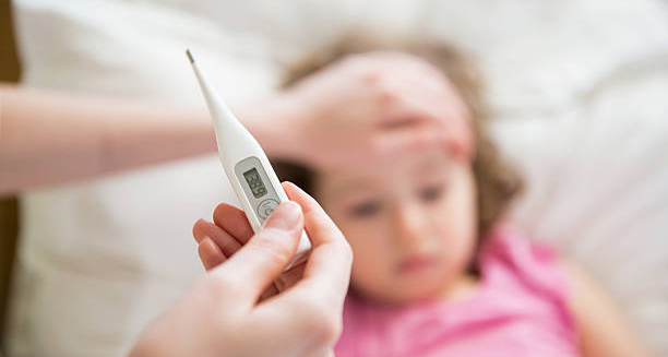 Digital thermometer showing fever in front of a sick child lying in bed