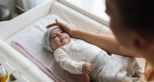 Mother gently caressing her baby’s head while the infant lies on a changing table, symbolising the care and attention involved in diagnosing cradle cap.
