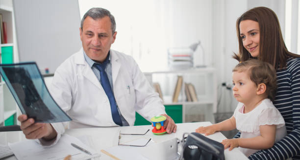Paediatric doctor showing an X-ray to a mother and child during a consultation, representing craniosynostosis diagnosis.