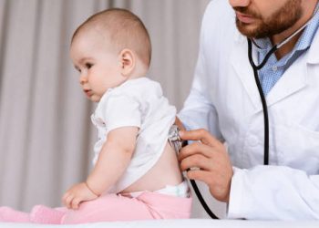 Paediatrician using a stethoscope to examine a baby’s back, assessing breathing to help diagnose croup.
