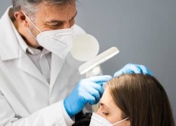 Dermatologist examining a patient's scalp for dandruff under a magnifying lamp