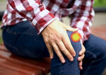 Man sitting on bench clutching knee with visible pain indicating dislocated kneecap