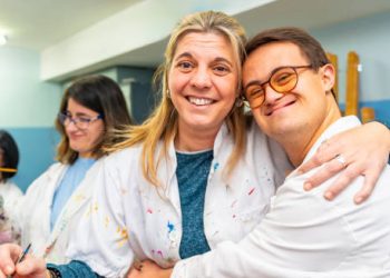 Smiling young adult with Down’s Syndrome hugging a caregiver in an art class