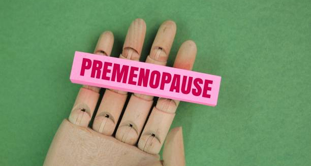 Wooden mannequin hand holding a pink label reading "Premenopause" on a green background