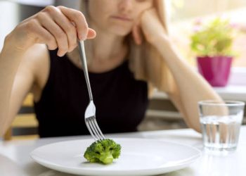 Woman looking at broccoli on a plate, showing signs of an eating disorder