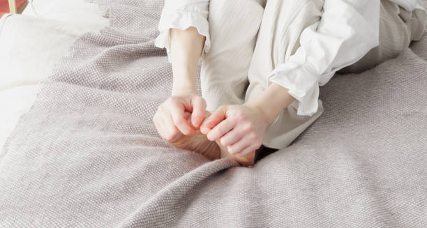 Person sitting on bed rubbing itchy toes due to chilblains