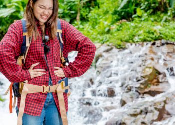 Woman holding stomach in discomfort during outdoor hike near waterfall