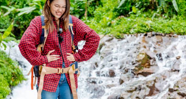 Woman holding stomach in discomfort during outdoor hike near waterfall