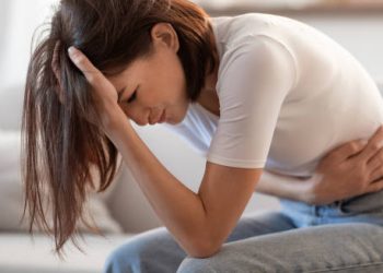 Woman clutching stomach and head in pain, showing symptoms of chronic pancreatitis.