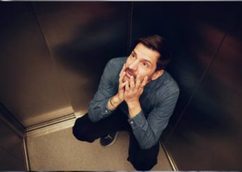 Anxious man crouching in lift showing symptoms of claustrophobia