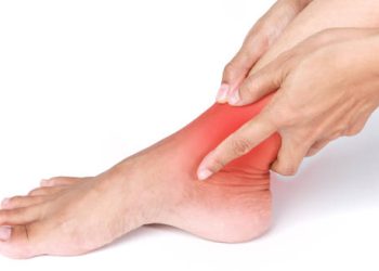 Person holding their inflamed ankle with visible redness indicating pain