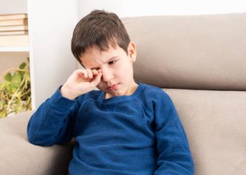 Child rubbing irritated eye showing early symptoms of conjunctivitis