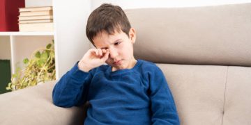 Child rubbing irritated eye showing early symptoms of conjunctivitis