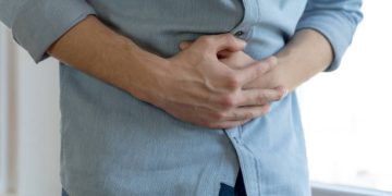 Man clutching his stomach experiencing abdominal discomfort, a common symptom of constipation.