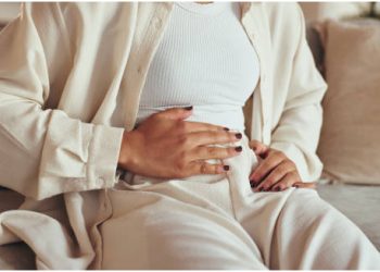 Person sitting on a couch holding their stomach, showing signs of abdominal discomfort.