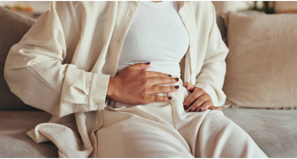Person sitting on a couch holding their stomach, showing signs of abdominal discomfort.