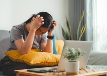 Frustrated woman scratching scalp while sitting on couch in front of laptop