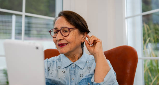 Elderly woman adjusting hearing aid while using a tablet