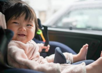 Smiling baby with short limbs sitting in a car seat