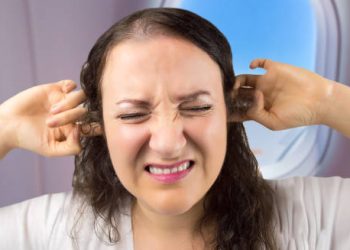 Woman experiencing ear discomfort on an aeroplane, showing symptoms of a burst eardrum