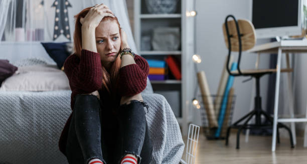 Distressed young woman sitting on the floor with her hands on her head in a bedroom
