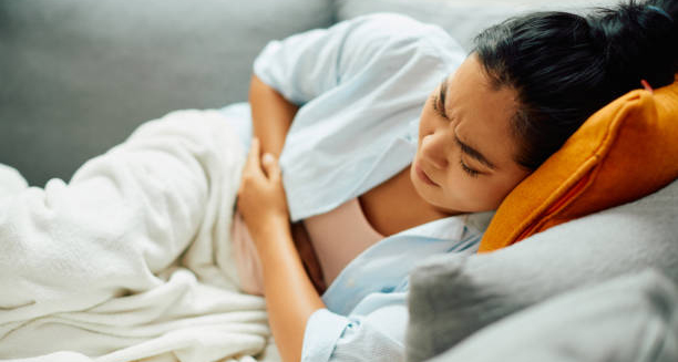 Woman lying on couch clutching her abdomen in pain, showing symptoms of endometriosis