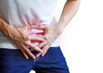 Man clutching lower abdomen in discomfort, indicating symptoms of enlarged prostate