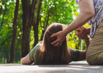Woman lying on ground during seizure while being helped, representing symptoms of epilepsy