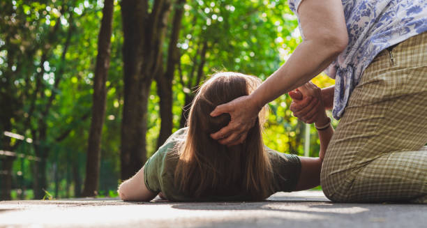 Woman lying on ground during seizure while being helped, representing symptoms of epilepsy
