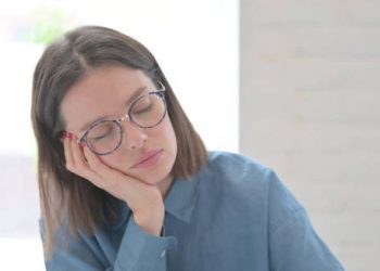 Young woman in glasses falling asleep at a desk during the day