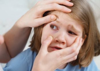 Adult examining young girl’s injured eye for signs of trauma
