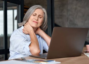 Older woman holding neck in pain while working on laptop