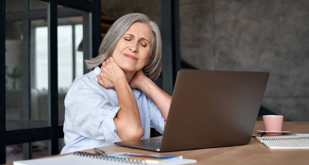 Older woman holding neck in pain while working on laptop