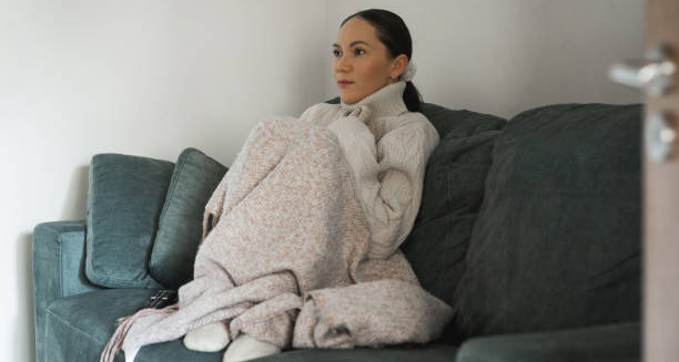 Woman wrapped in a blanket sitting on a couch to treat chilblains